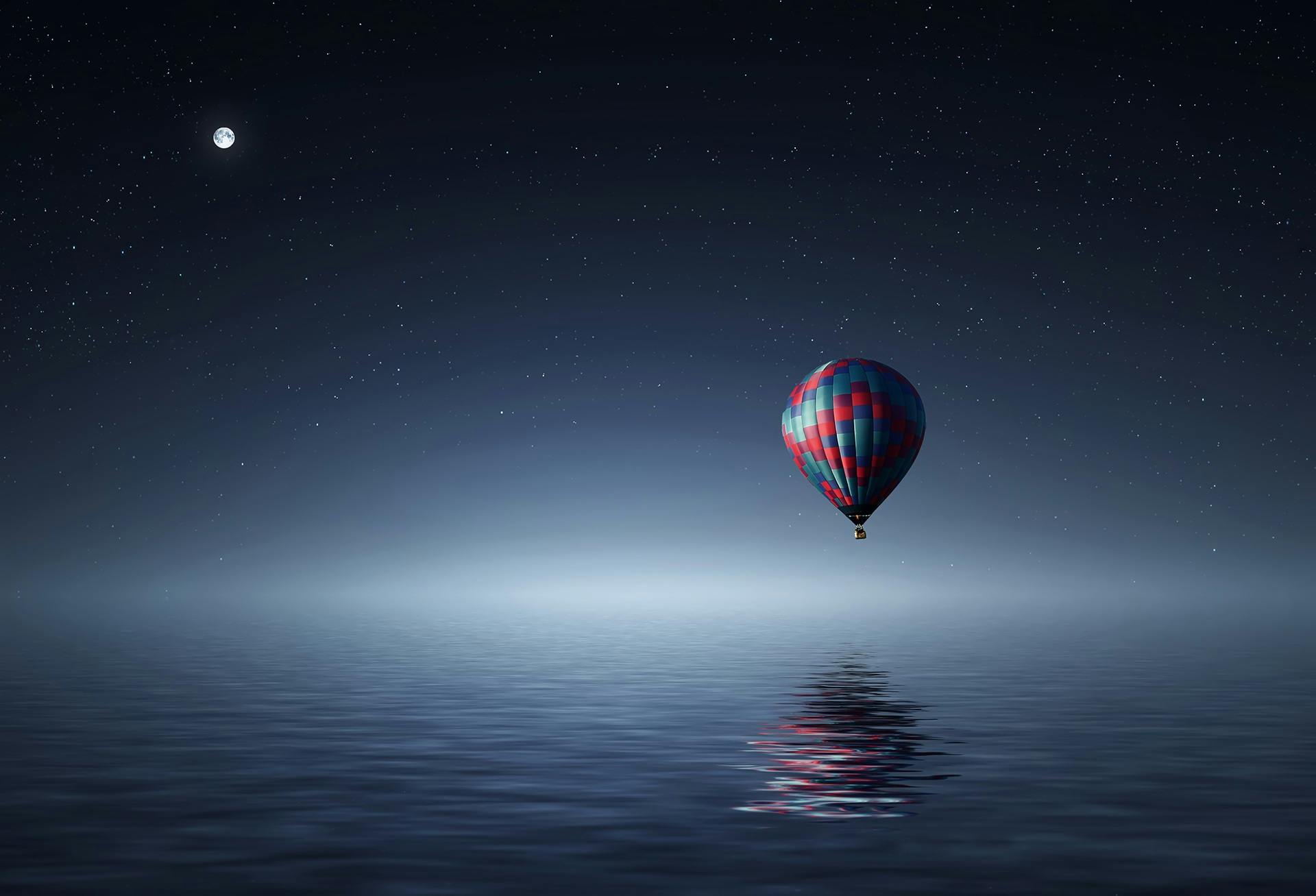 A air balloon is sailing in a large sea at night when the moon is full and the stars are twinkling
